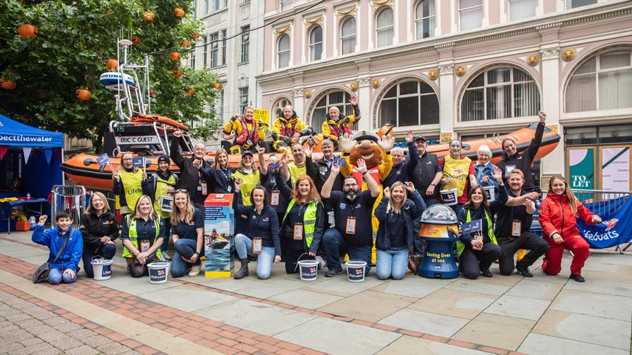 The RNLI family – fundraisers, supporters, crew and other volunteers – line up with a B class lifeboat, recreating the first fundraising street collection, that took place in Manchester in 1891