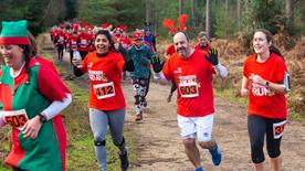 Runners taking part in an RNLI Reindeer Run in Moors Valley Country Park in Dorset. Most runners are wearing red Reindeer Run T-shirts and antlers. Two are waving at the camera.
