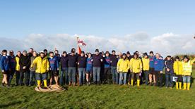 A group photo of Hoylake RNLI volunteers and members of Hoylake Sailing Club who took part in the 50th Slater Trophy Boxing Day Tug of War in 2022. They are standing outdoors on grass and the sky is blue.