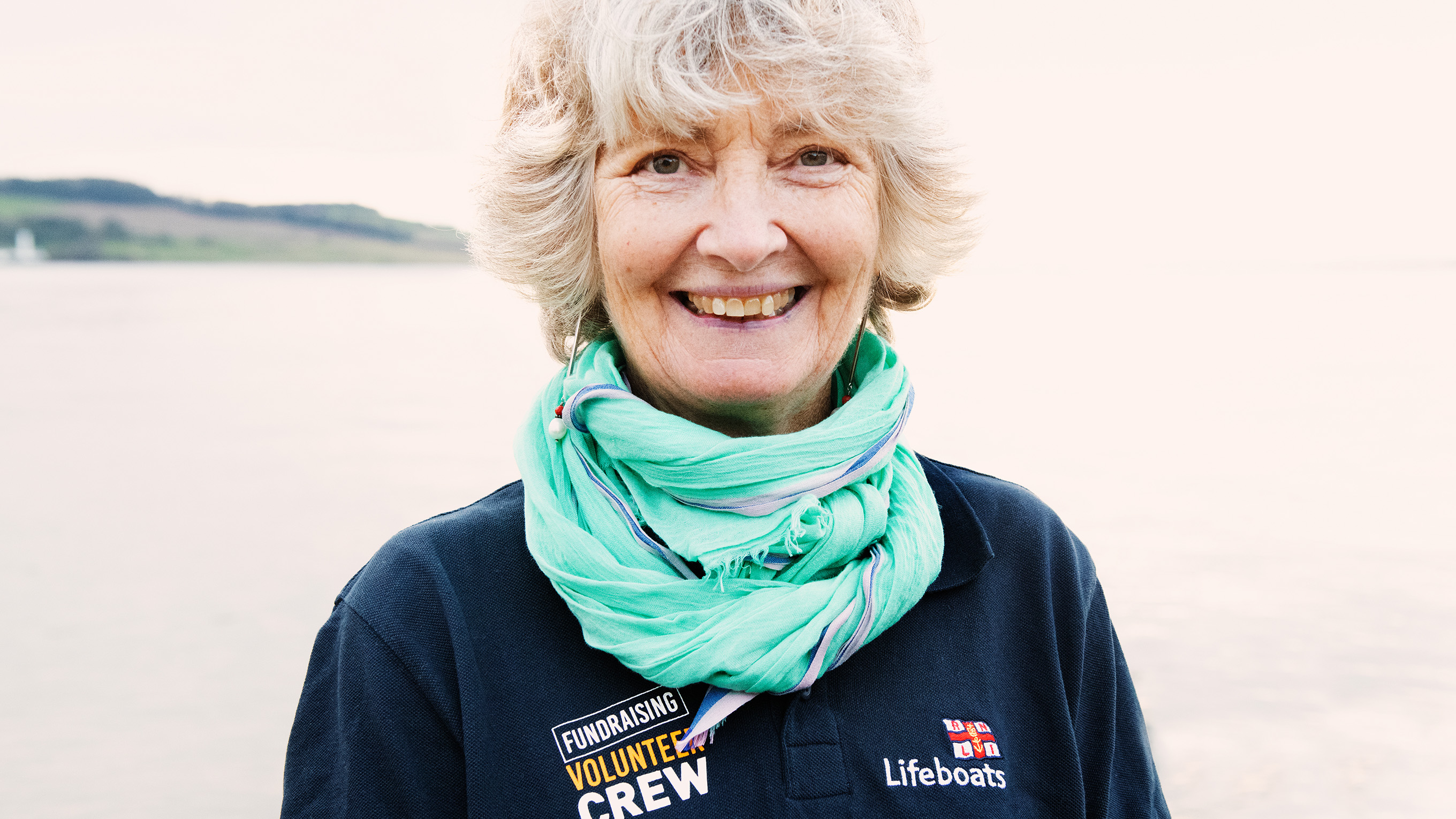 Close-up of a fundraising volunteer wearing an RNLI branded polo shirt and a light blue scarf.