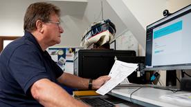 A volunteer working on a computer. There is a model lifeboat on top of a filing cabinet in the background.