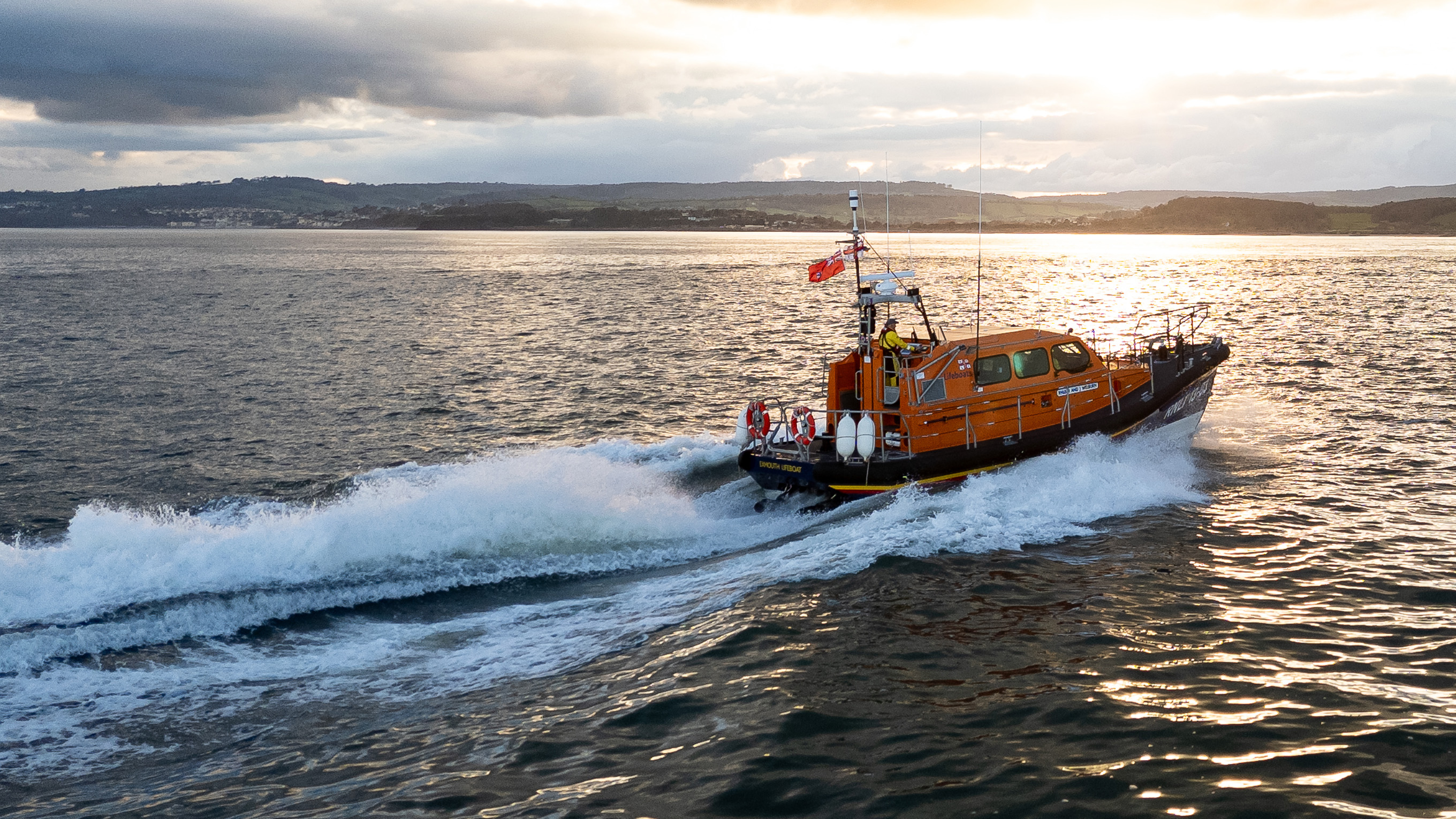 A lifeboat powering out to sea at sunset.