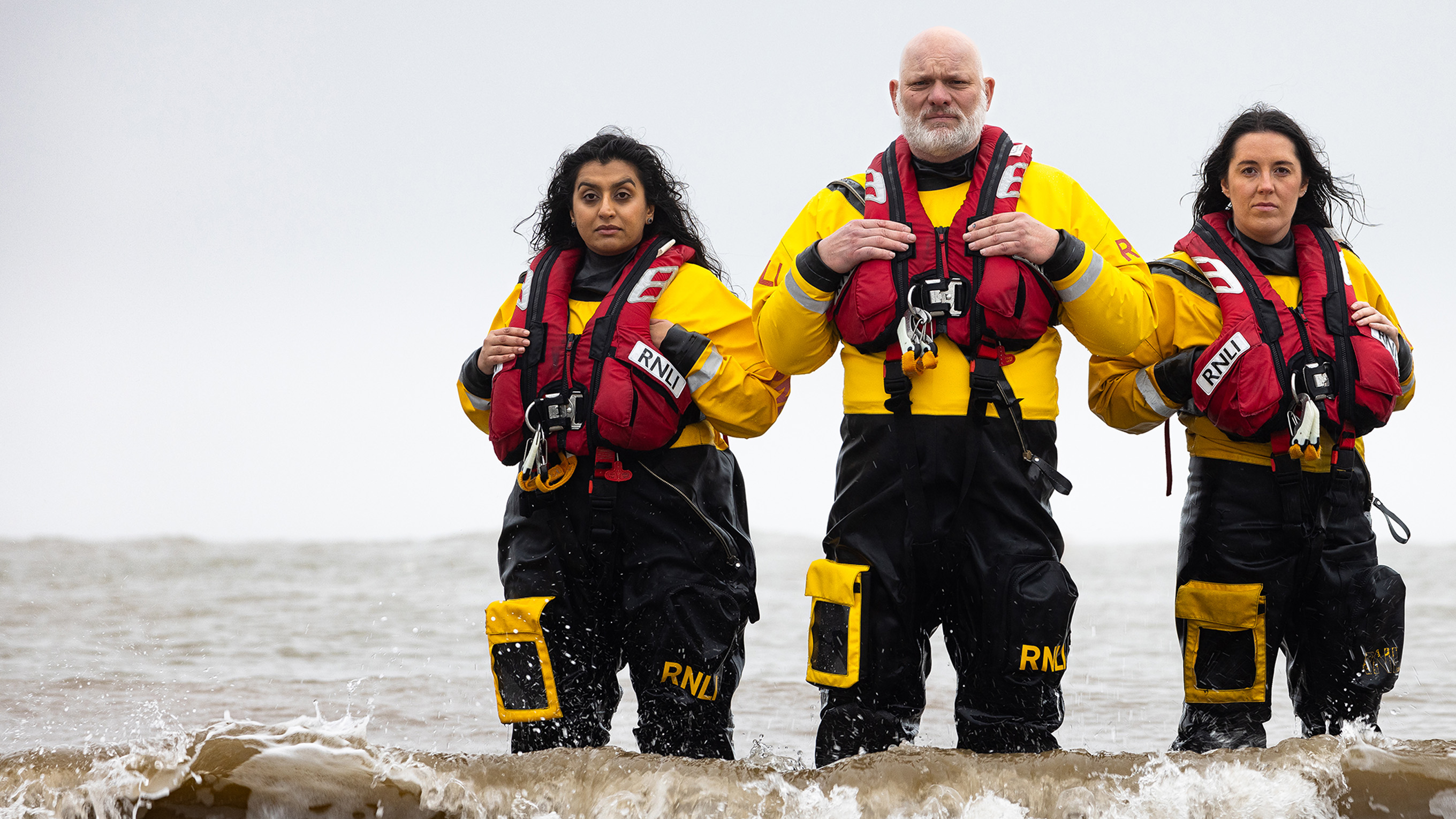Group shot of RNLI volunteer crew in ILB kit standing in the sea, shot in Lyme Regis