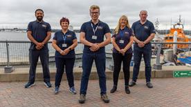 A group of RNLI volunteers stood on the pavement outside the RNLI College in Poole.