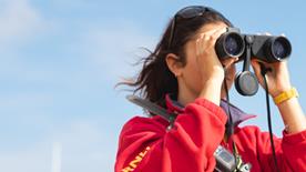 A close-up of a female lifeguard looking through binoculars out to sea.
