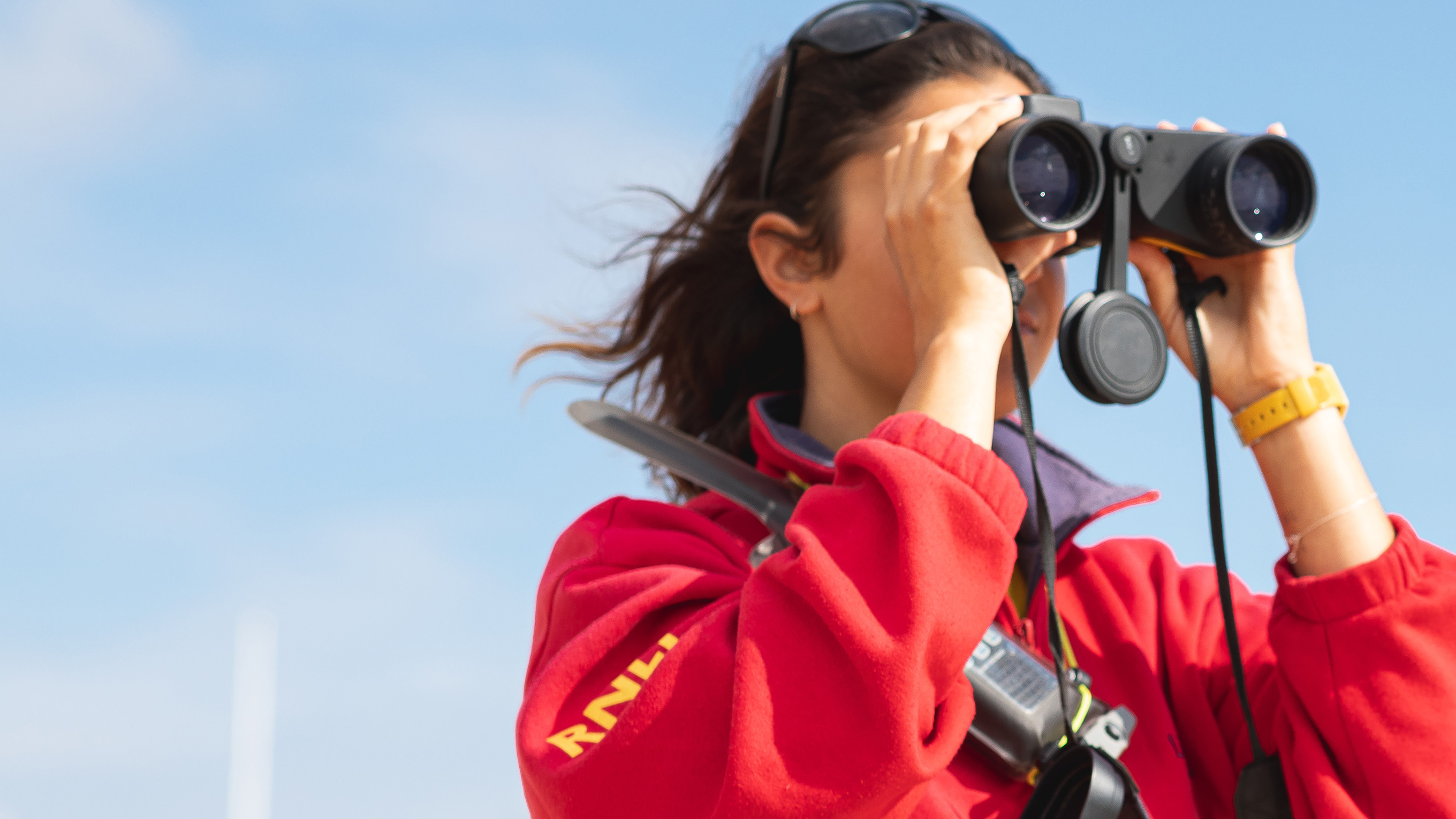 A close-up of a female lifeguard looking through binoculars out to sea.