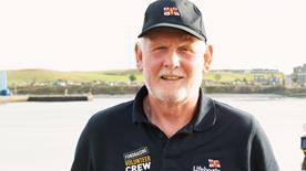A fundraising volunteer smiling at the camera. He is wearing an RNLI branded polo shirt and cap.