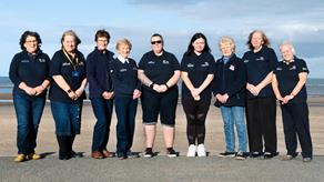 A group of nine RNLI fundraisers stand on a beach