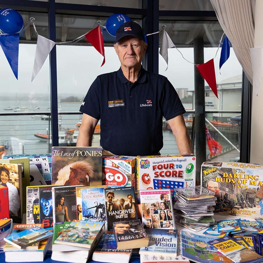 RNLI volunteer with a charity stall of items to sell facing the camera