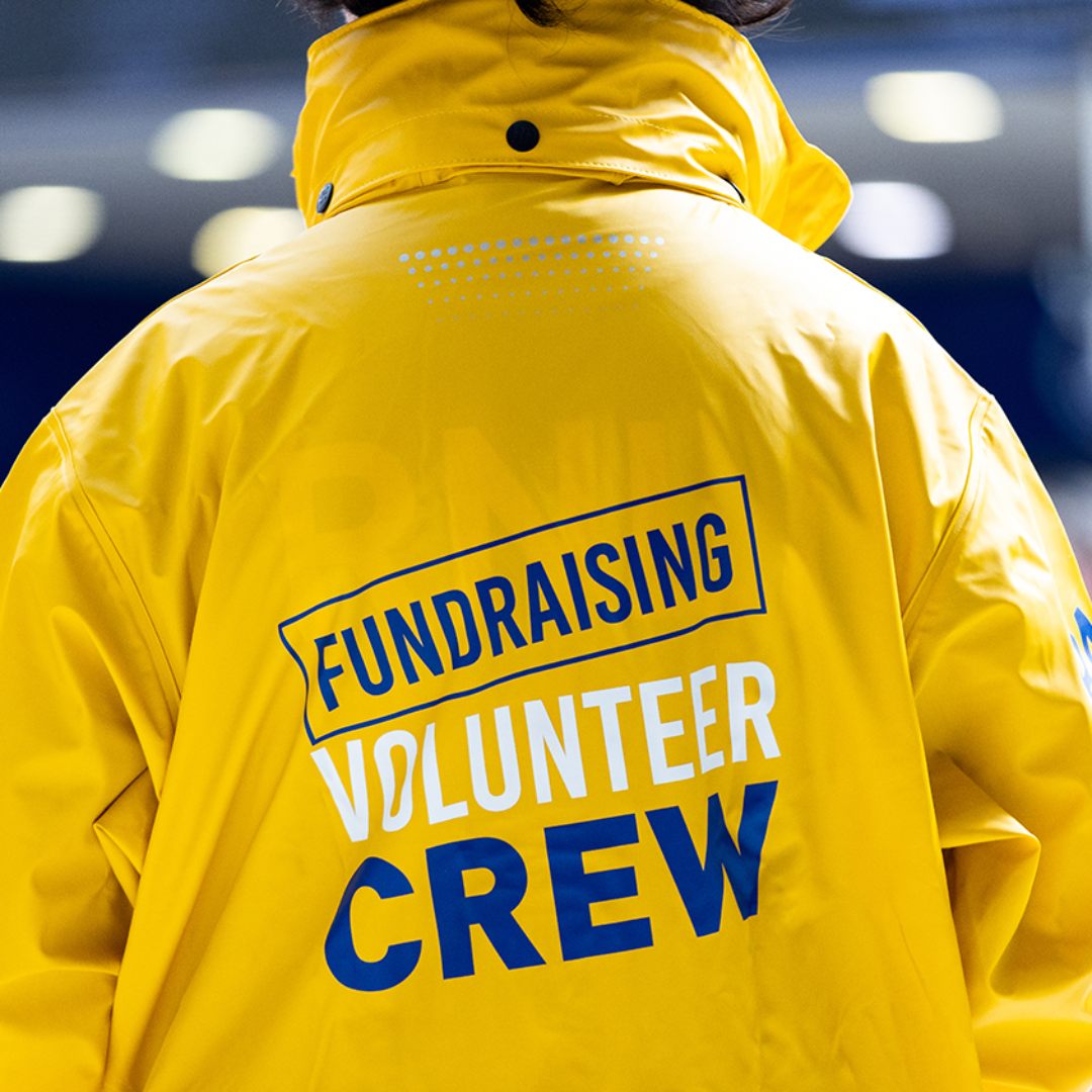 RNLI fundraising volunteer wearing a yellow jacket with their back to the camera
