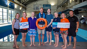 The RNLI Executive Team promoting find your float for World Drowning Prevention Day 2025, standing by a pool and holding flotation devices and signs