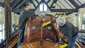 Two volunteers cleaning a historic mahogany lifeboat