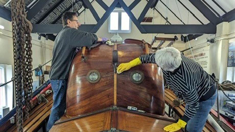 Two volunteers cleaning a historic mahogany lifeboat