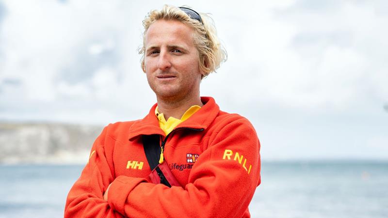 Jake Dean RNLI lifeguard standing in crew kit on beach