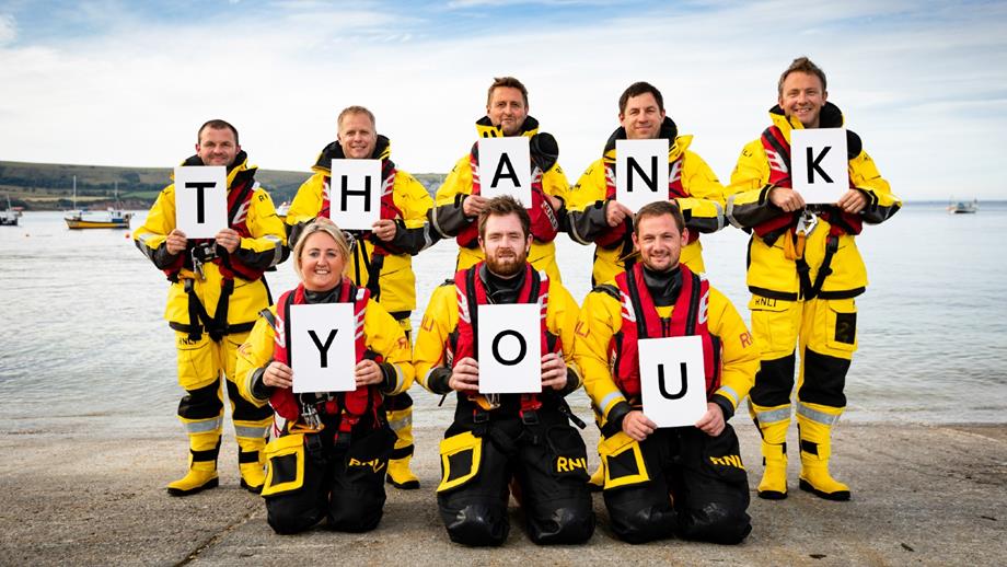 Lifeboat crew members are smiling and holding cards that read ‘thank you’