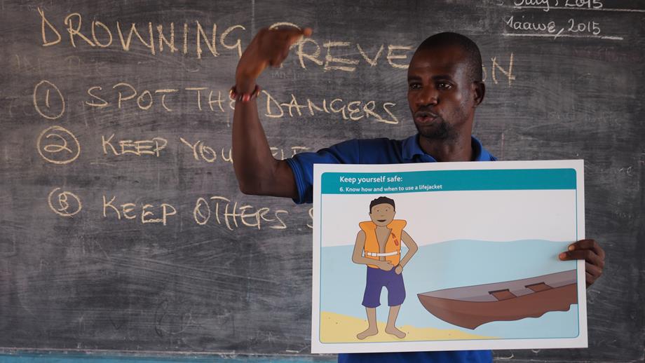A teacher in Ghana holding up a water safety message sign