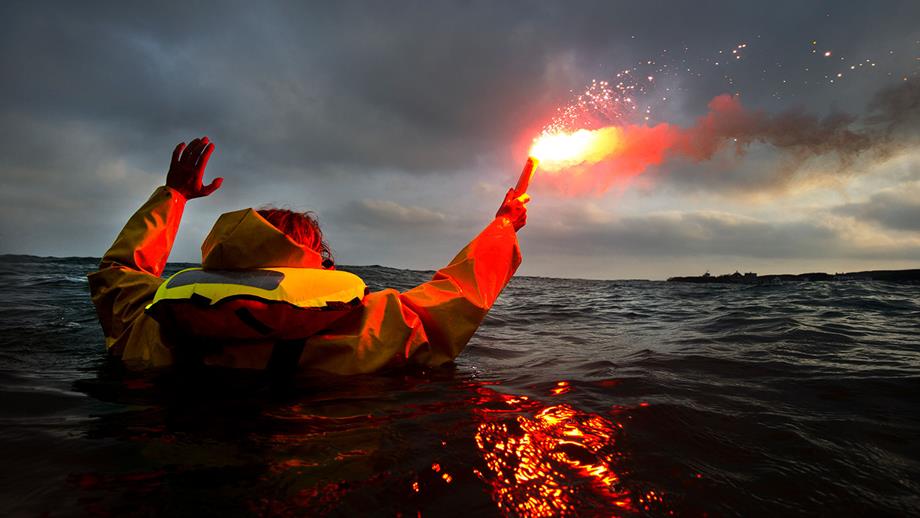 A person in the water wearing a life jacket holding a lit flare