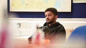 A young black man attentively watches an RNLI training session in a classroom at the University of Portsmouth.