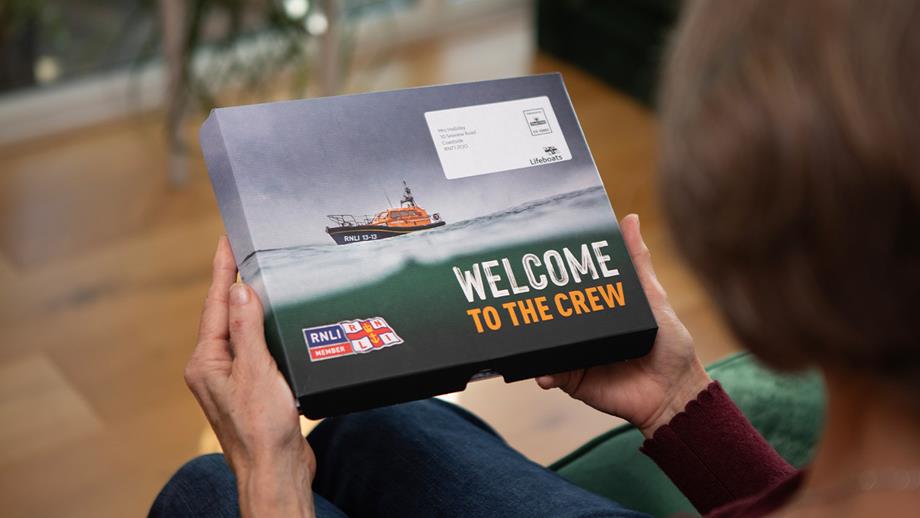 Two hands holding an RNLI membership pack, which reads: 'Welcome to the crew'