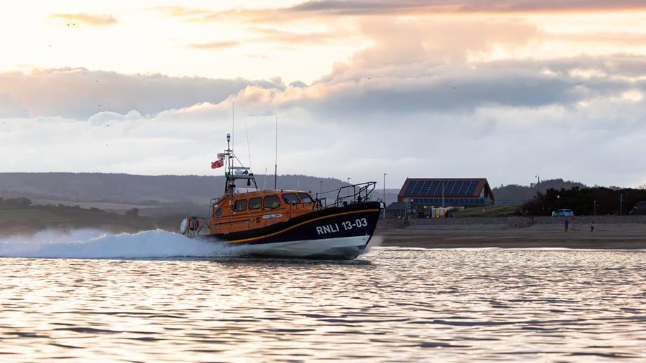 RNLI Exmouth LIfeboat 13-03 going out on a lifesaving mission with the RNLI Exmouth Lifeboat Station in the background.